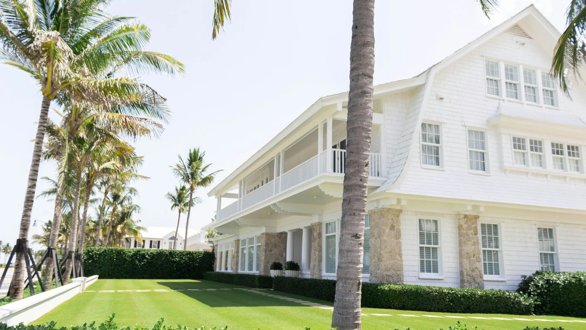 A large white two-storey Florida home with a wraparound porch, framed by palm trees and a manicured lawn