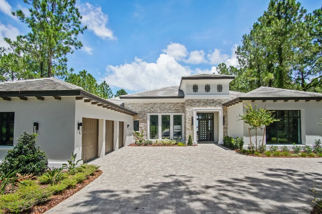 A single-storey Southwest Florida home with a stone façade and paver driveway, framed by pines.