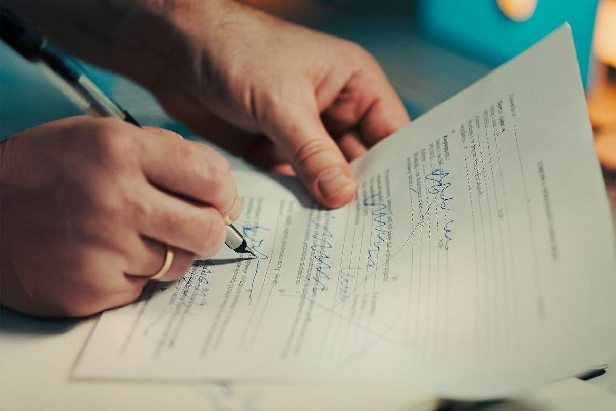 A hand signing a printed contract on a desk