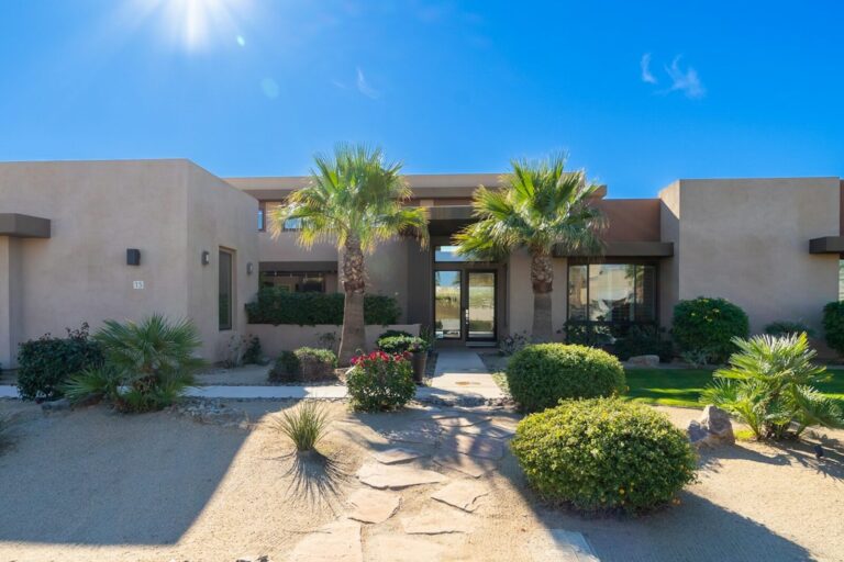 A single-storey stucco house with palms either side of the front door