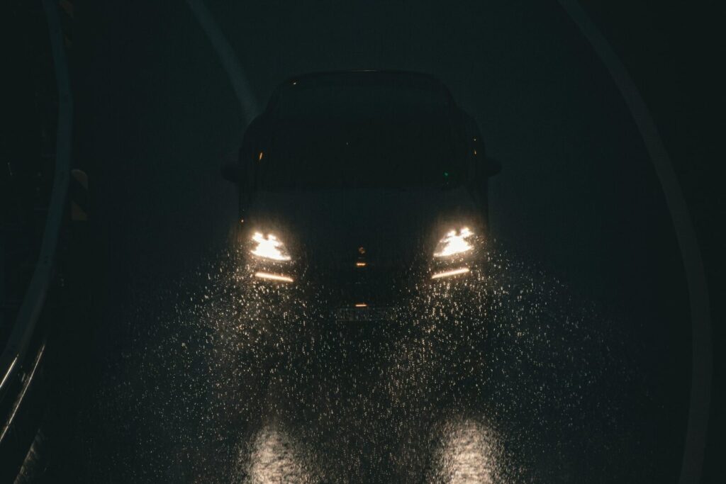 Headlights on a wet road at night, seen from behind another car