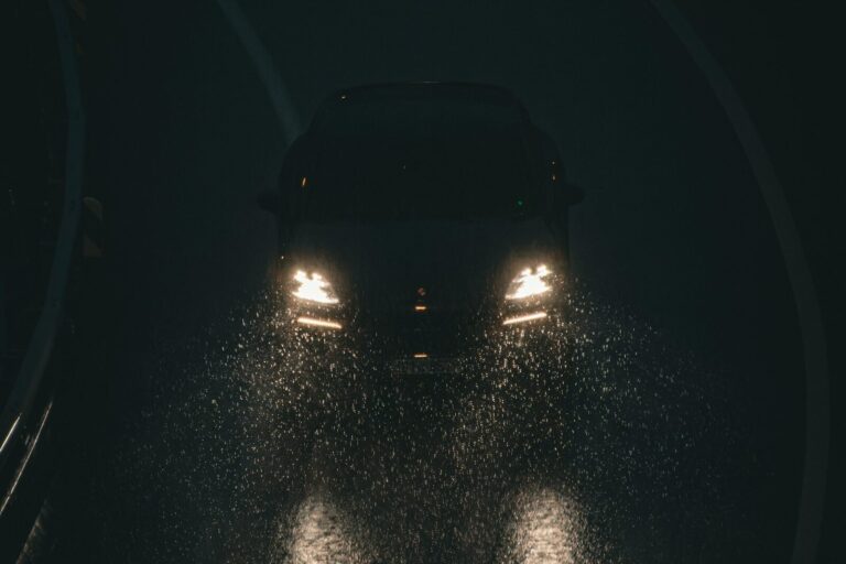 Headlights on a wet road at night, seen from behind another car