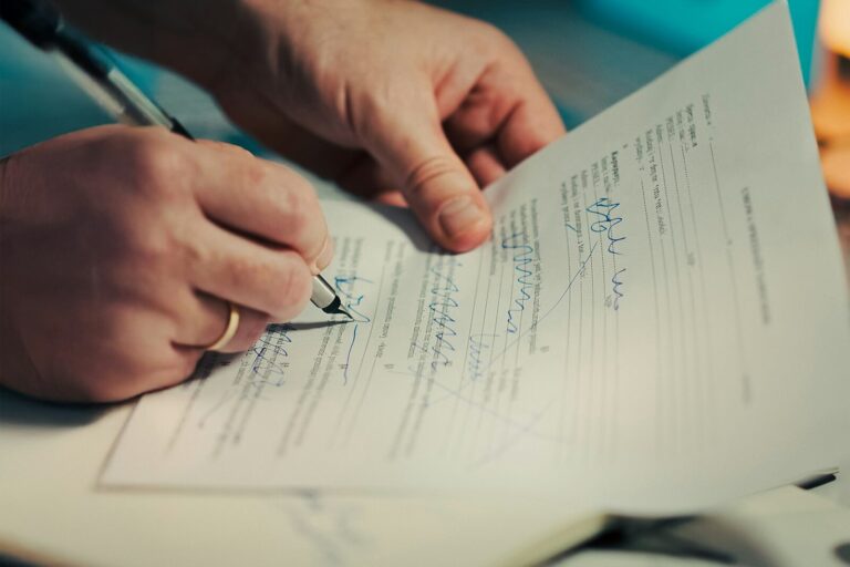 A hand signing the last page of a printed agreement with a fountain pen