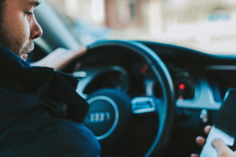 A driver holding a phone at the wheel of a car, dashboard lit