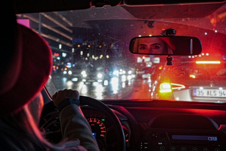 A driver at the wheel in heavy rain, traffic and tail lights ahead through the windscreen