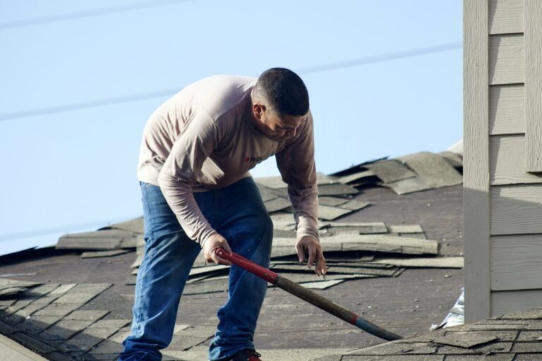 A roofer levering old shingles off a roof deck with a flat bar