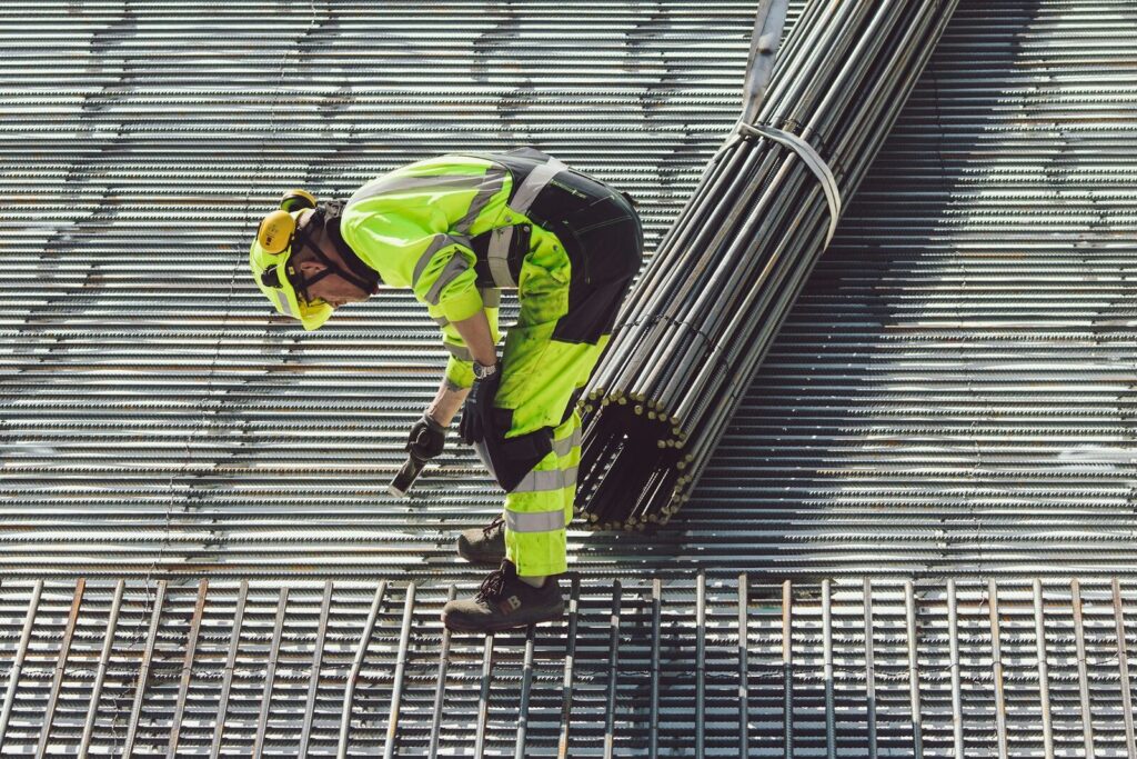 Un trabajador de construcción con ropa de alta visibilidad cargando varilla de acero en obra